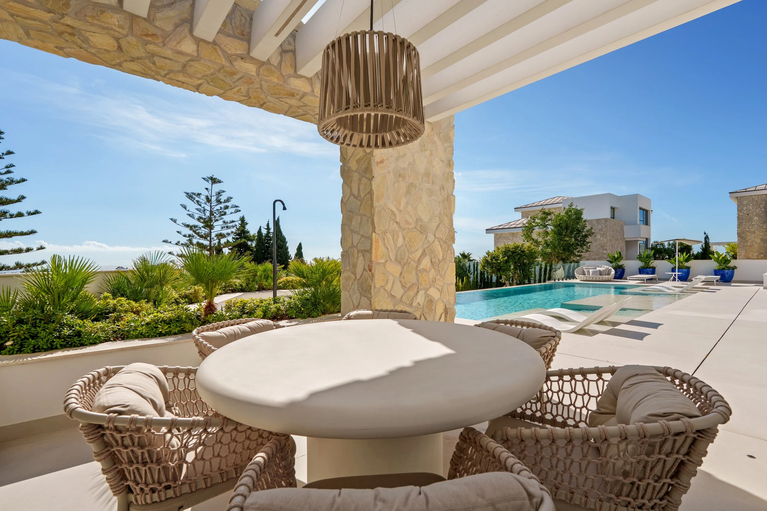 A covered terrace featuring a built-in outdoor kitchen, a formal dining area, and a relaxed lounge space, all overlooking the pool and valley.