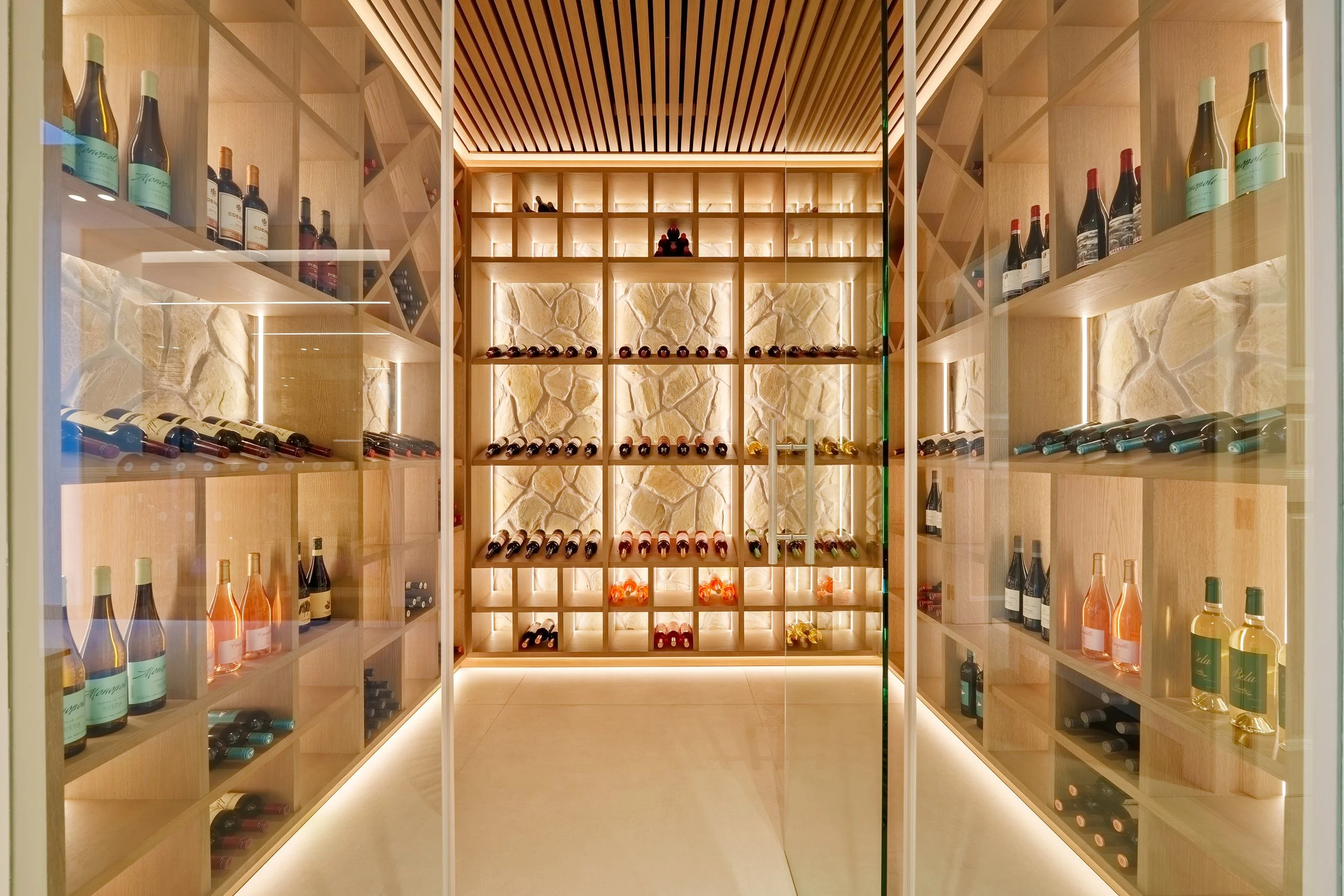 A glass-enclosed, climate-controlled bodega with custom back-lit shelving for a private collection.