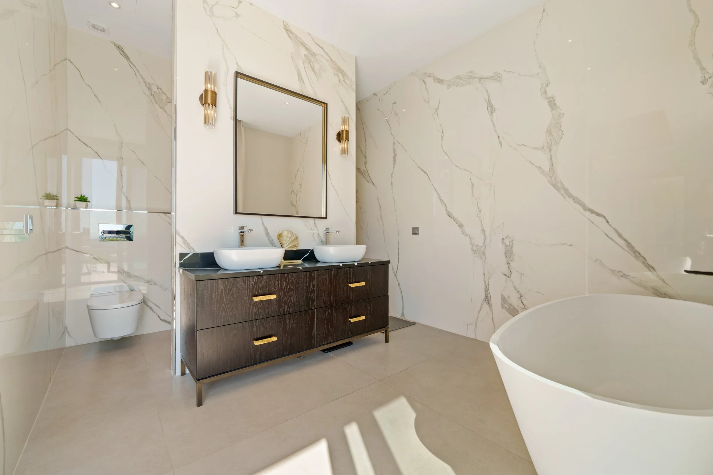 Contemporary bathroom finished in floor-to-ceiling marble with a double vanity and freestanding tub.