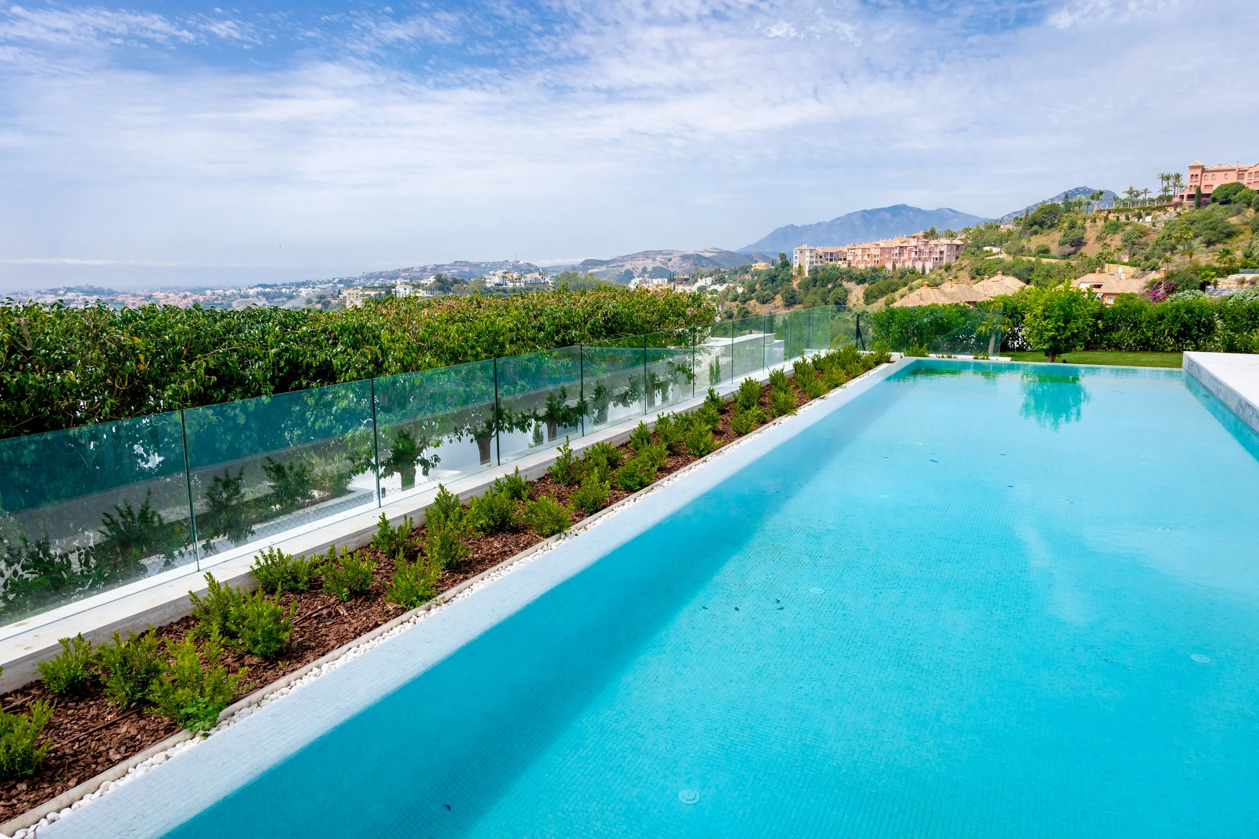 Close-up of an infinity pool edge overlooking the Mediterranean coastline and green hills.