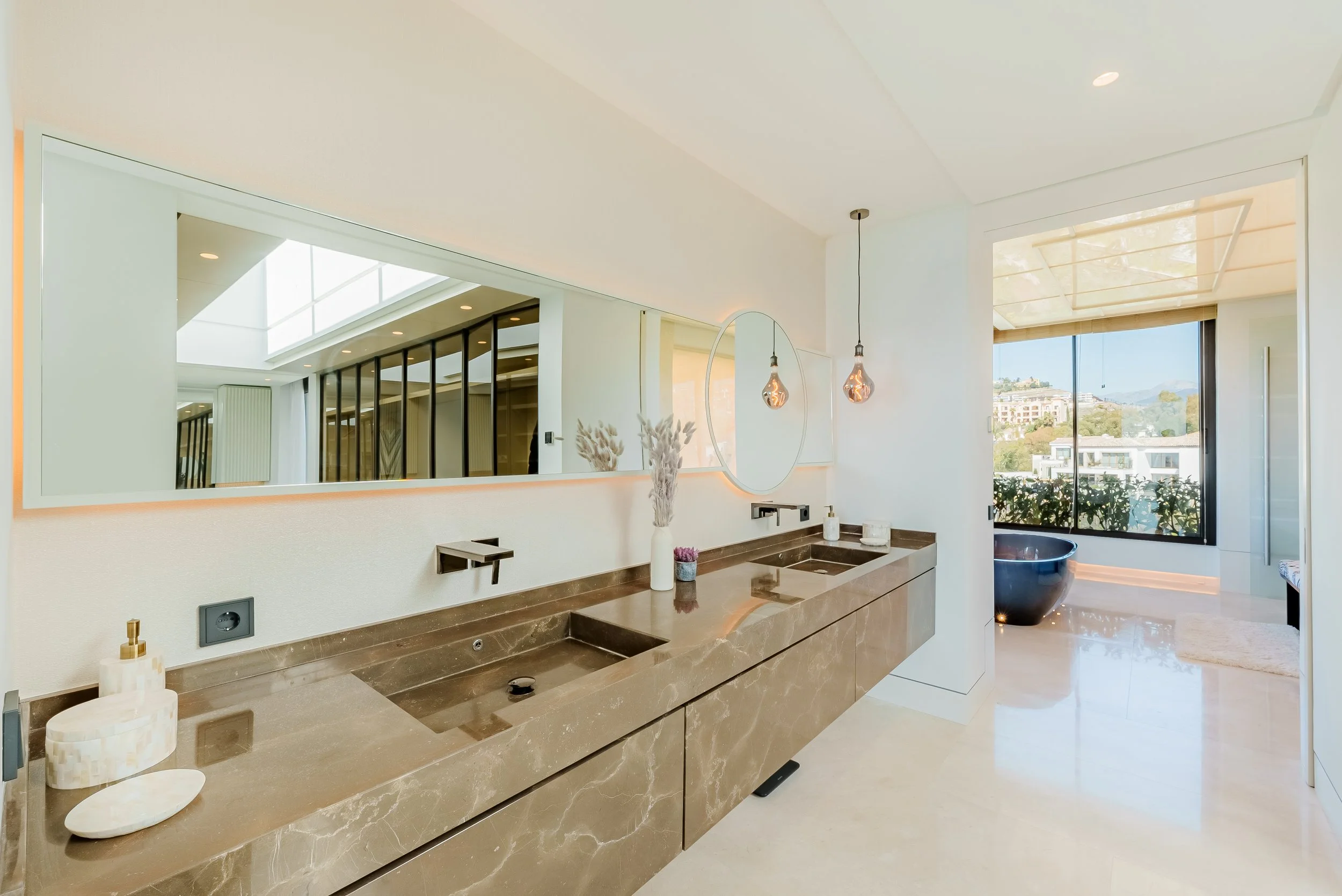 Elegant bathroom featuring a long natural stone double vanity and expansive mirrors.