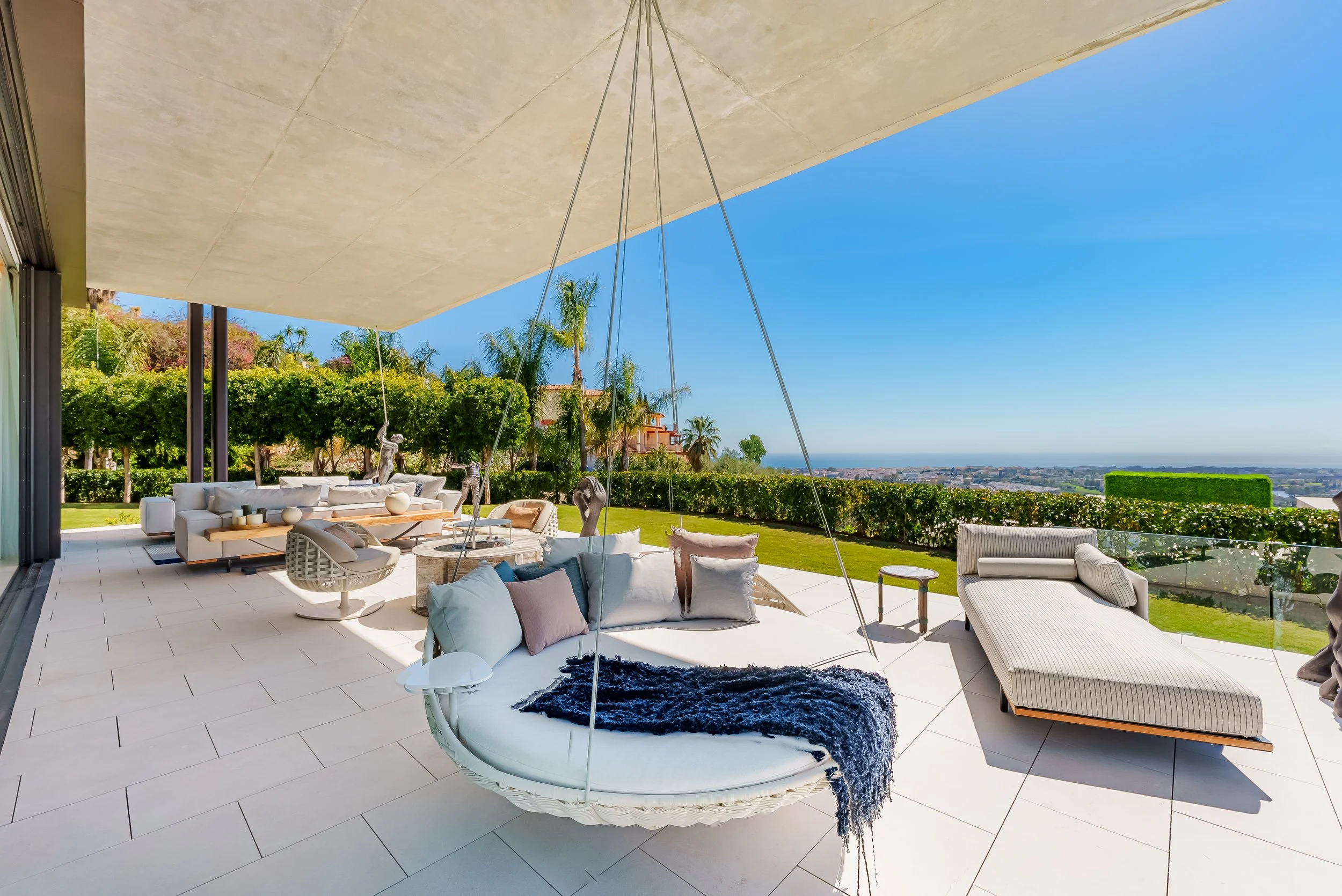 Covered terrace with plush outdoor sofas and a modern silver sculpture overlooking the garden.