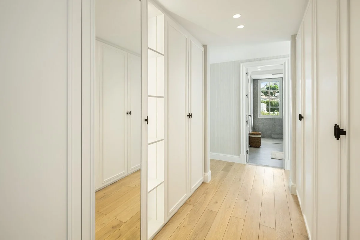 Minimalist walk-in dressing room with custom white cabinetry and warm wood flooring.