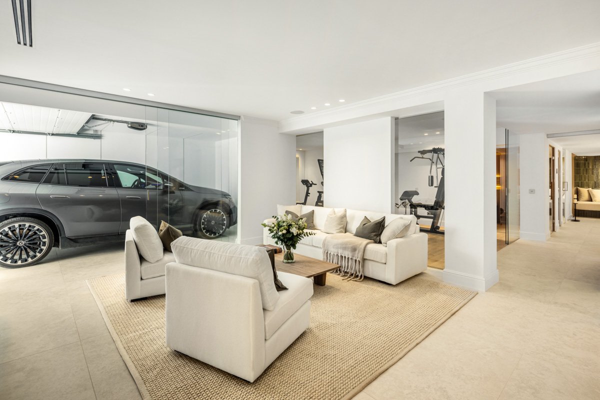Private garage with glass partitions showing a luxury vehicle adjacent to a lounge and gym area.