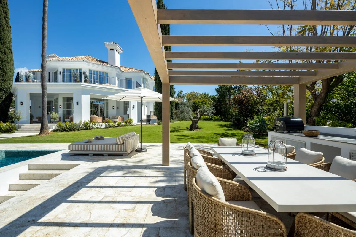 Outdoor al fresco dining area under a modern pergola overlooking the pool and gardens