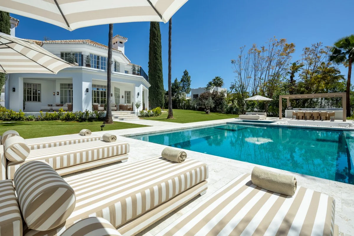Elevated view of a luxury pool area with striped sun loungers and a sunken firepit lounge.