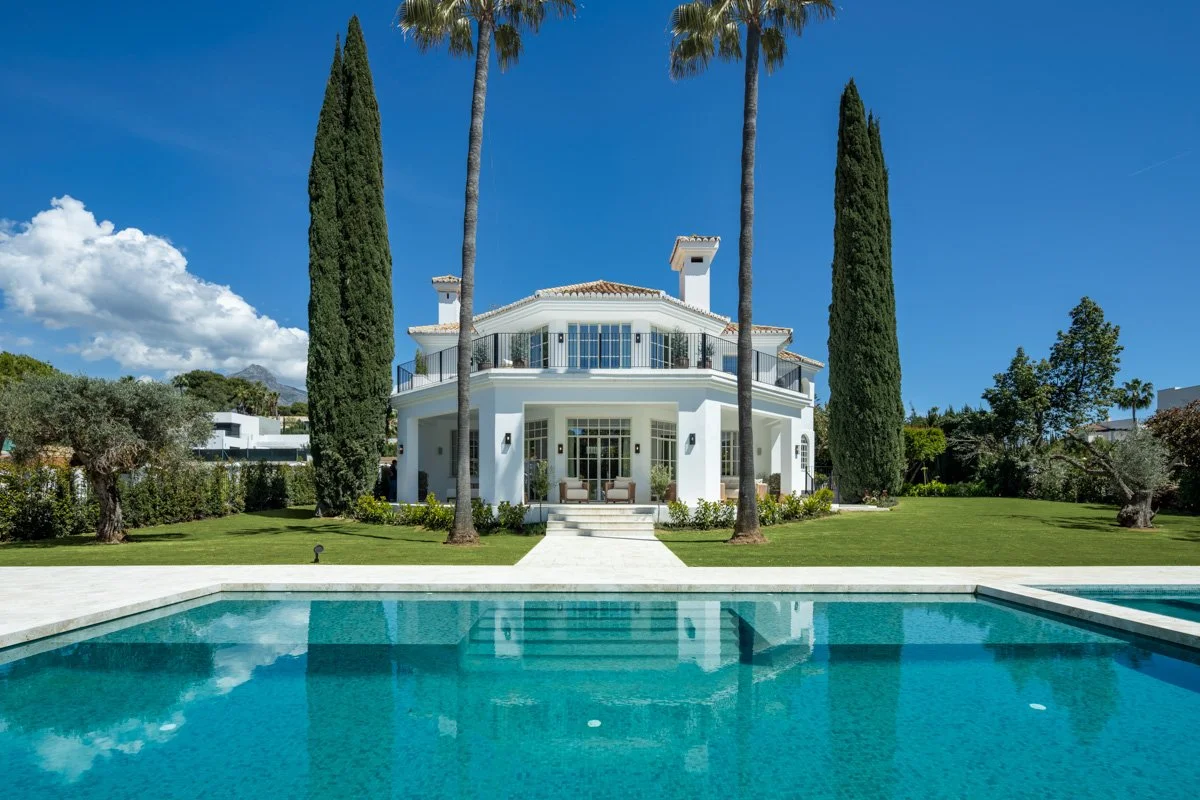Luxury villa CMH614563S exterior in Nueva Andalucia featuring a large swimming pool and tall cypress trees.