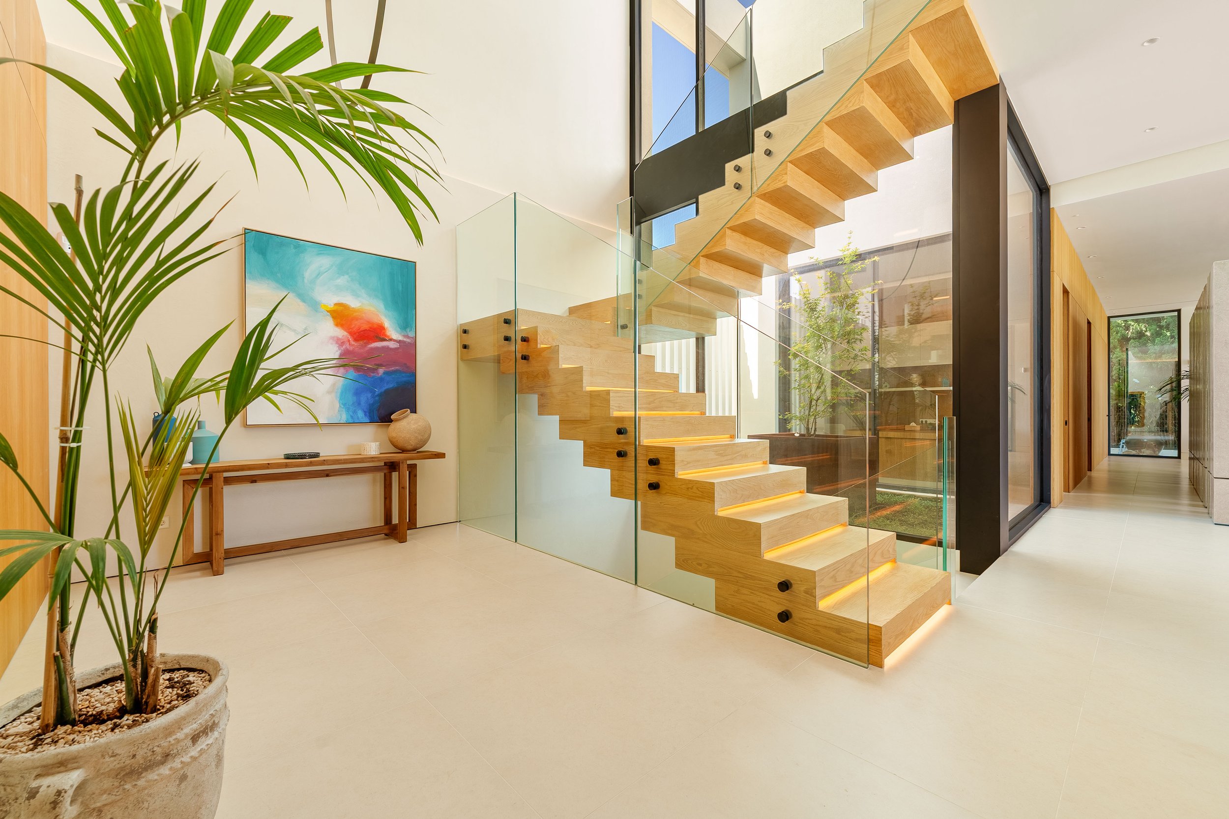 Architectural floating wooden staircase with glass balustrades and double-height ceiling.