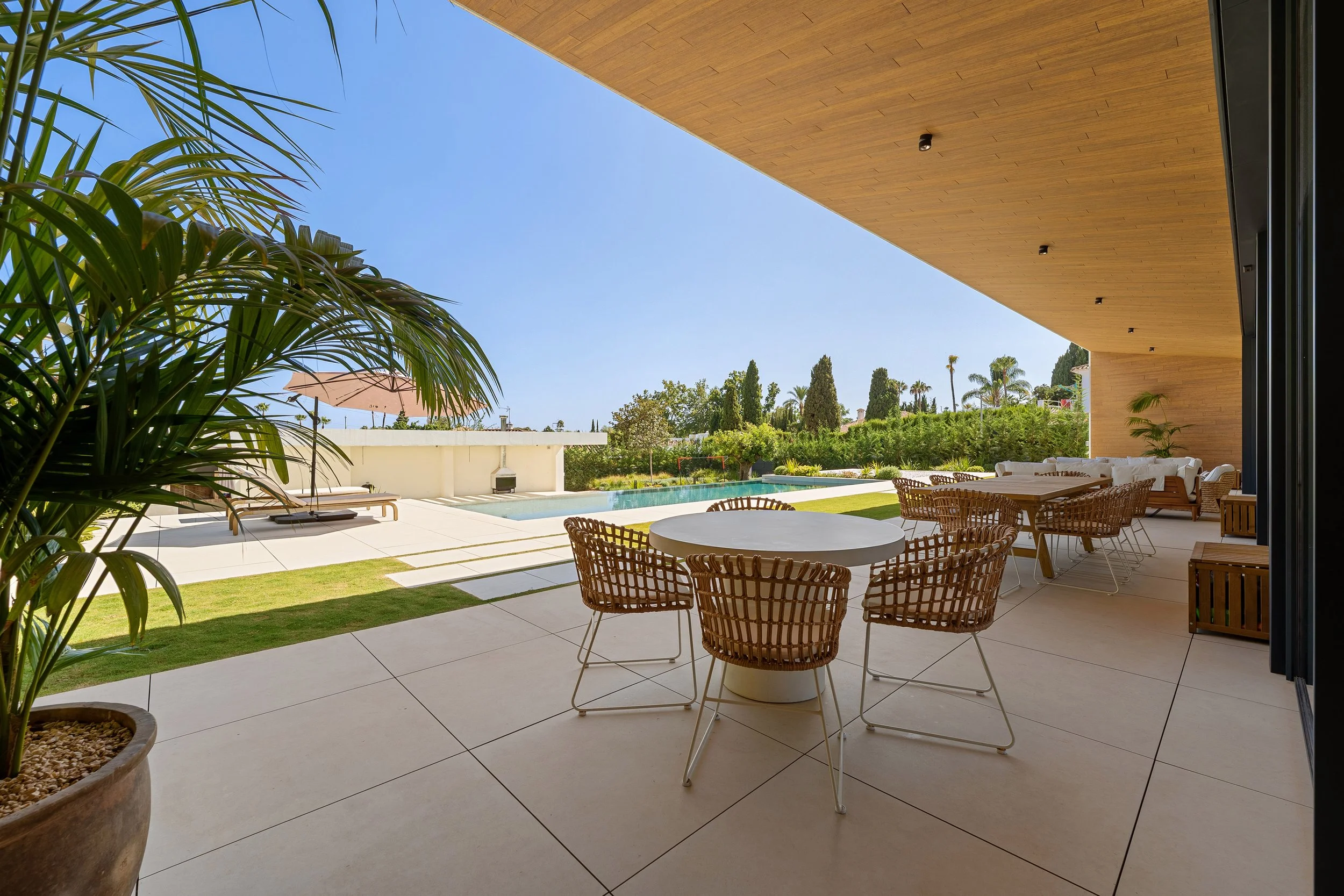 Spacious covered terrace with luxury outdoor lounge furniture, wooden ceiling details, and views of the private pool.