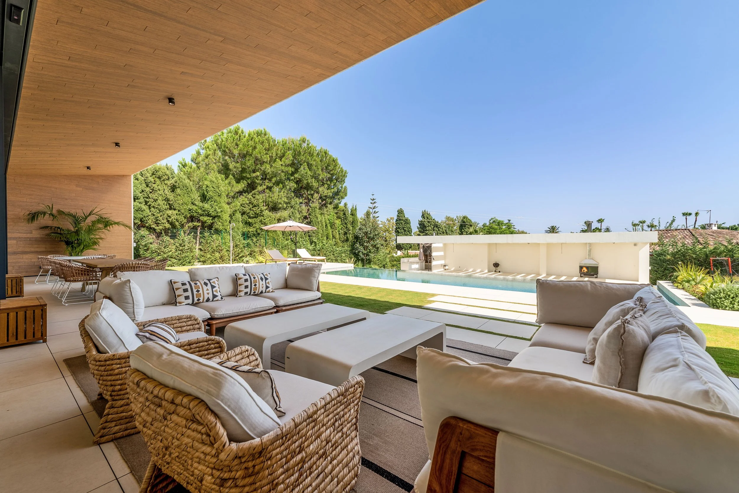 Shaded outdoor seating area with high-quality wicker furniture overlooking the garden and pool.