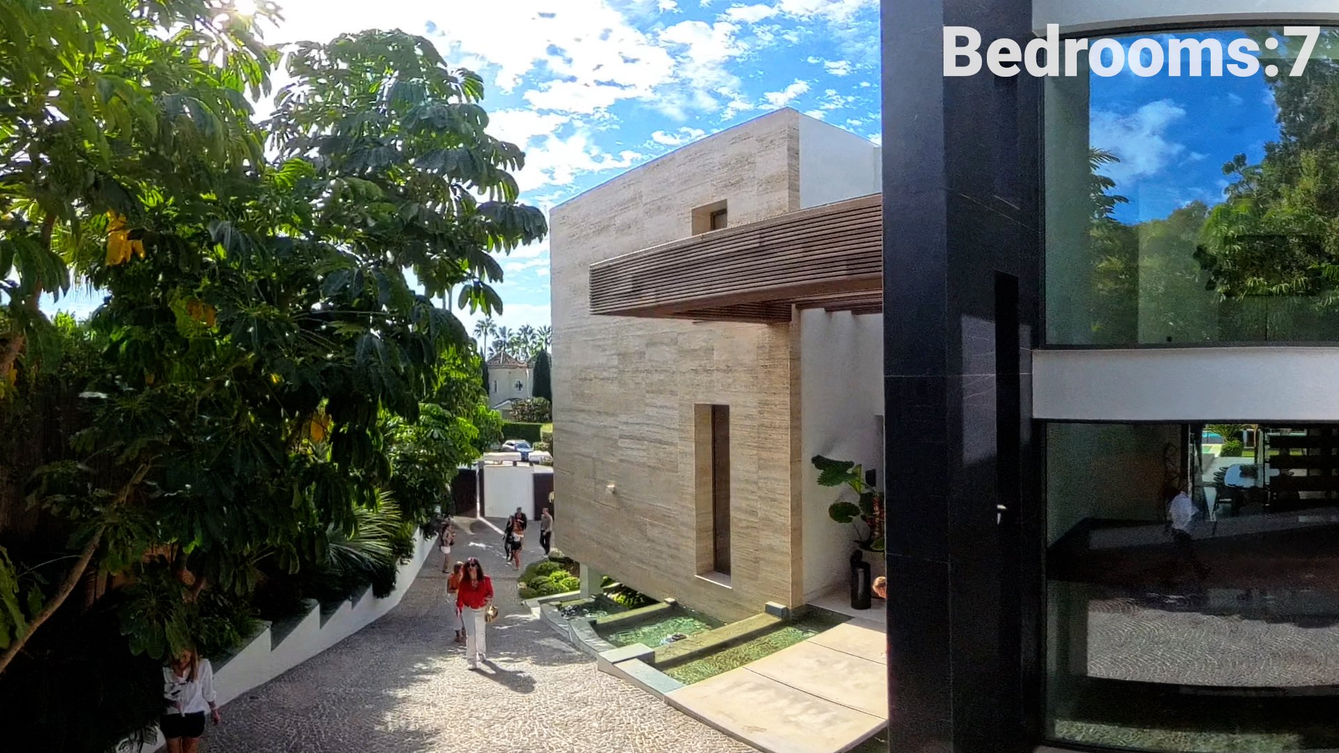 Screen capture from the 2025 Open House showing the modern architectural facade of Villa CMH2265S in Sierra Blanca, with an attendee walking past the stone entrance