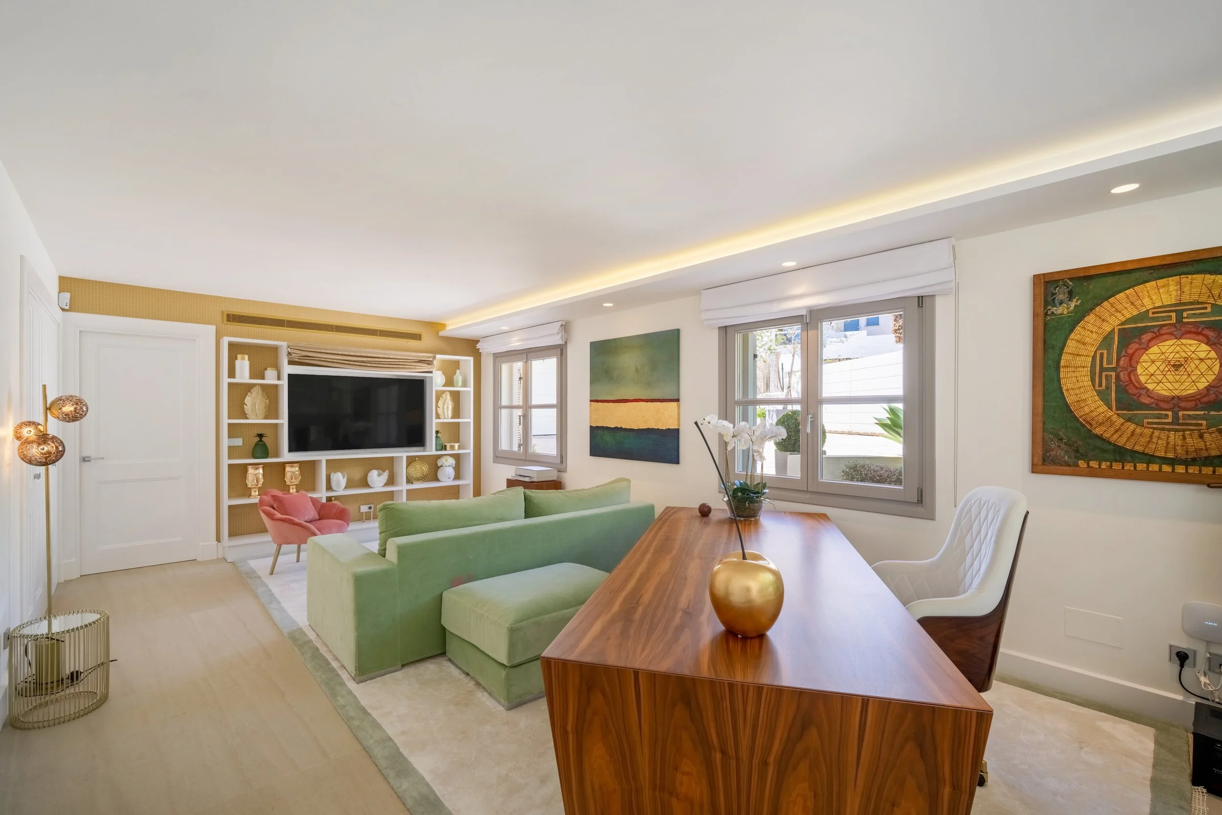Stylish contemporary home office with a rich wood desk, comfortable green seating area, and integrated shelving units.