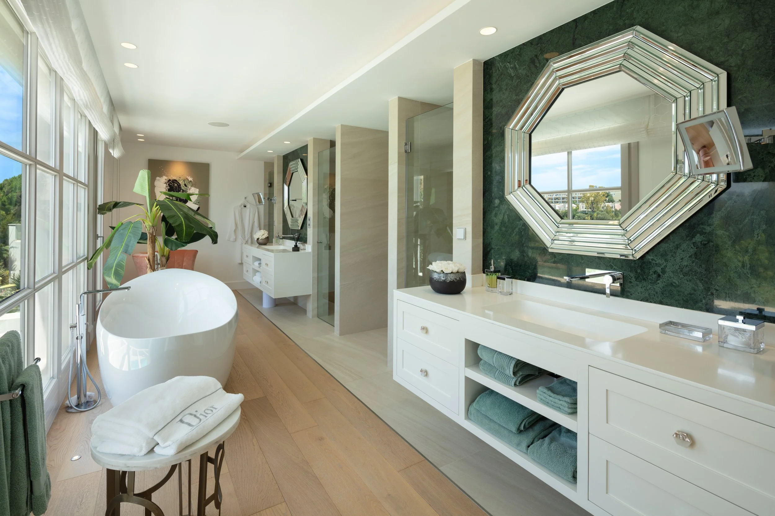 High-end bathroom featuring dual vessel sinks, large geometric mirrors, marble wall cladding, and a sleek modern soaking tub.