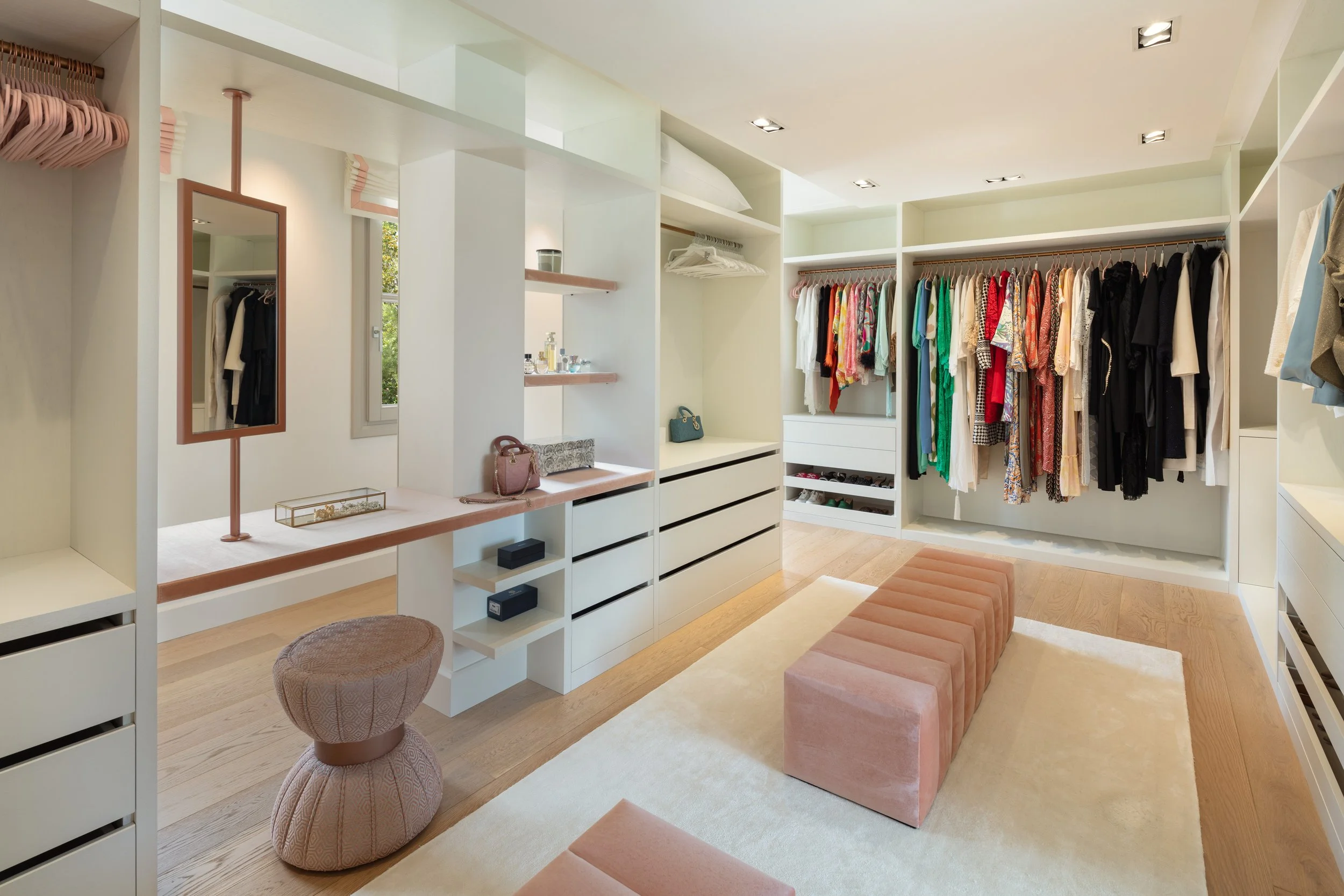 Expansive walk-in dressing room with custom white cabinetry, central seating bench, and organized boutique-style clothing displays.
