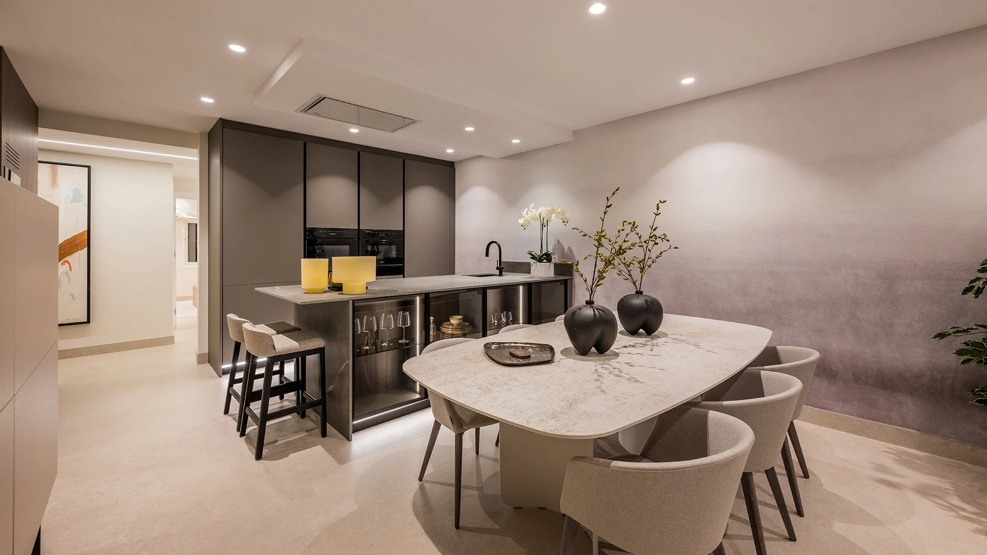 Gourmet kitchen with dark cabinetry and a minimalist oval dining table for high-end entertaining.