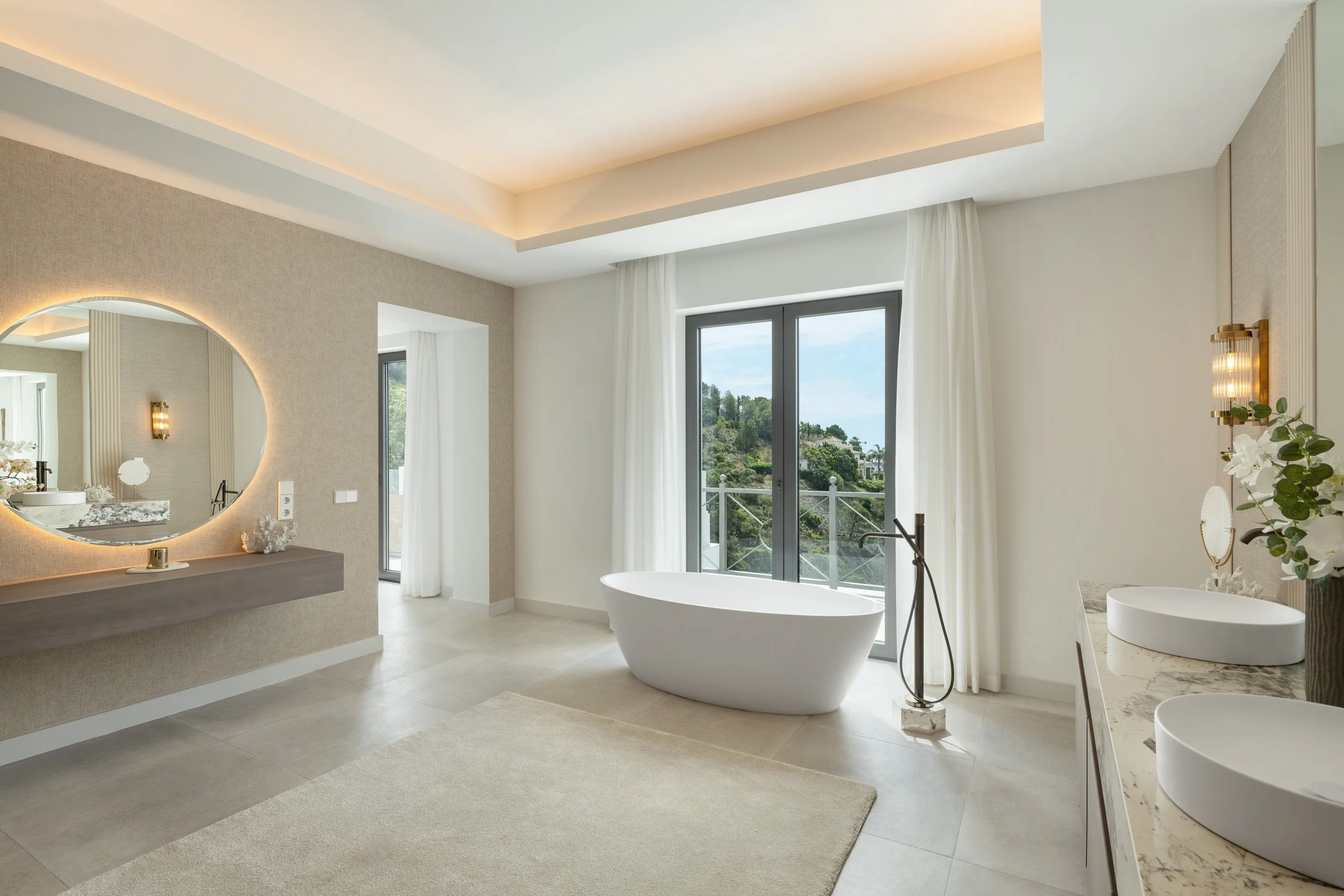 A luxurious master bathroom equipped with a freestanding soaking tub and modern vanity, overlooking the green landscape.