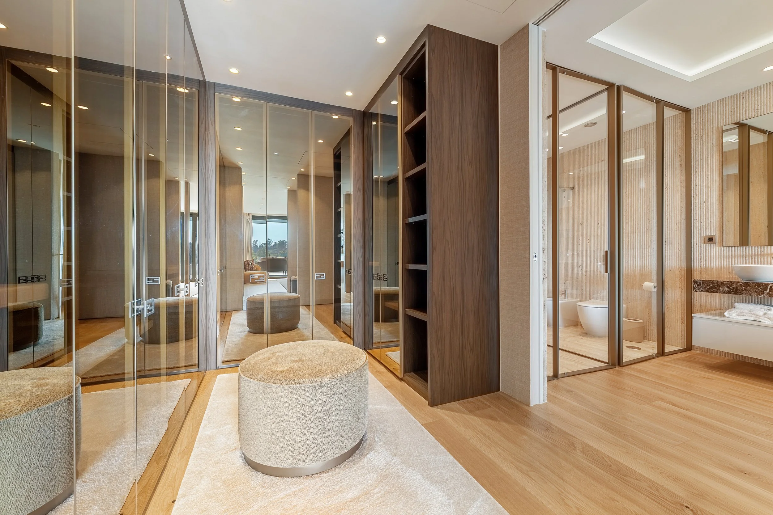 Spacious custom-built dressing room with integrated lighting and glass wardrobes.
