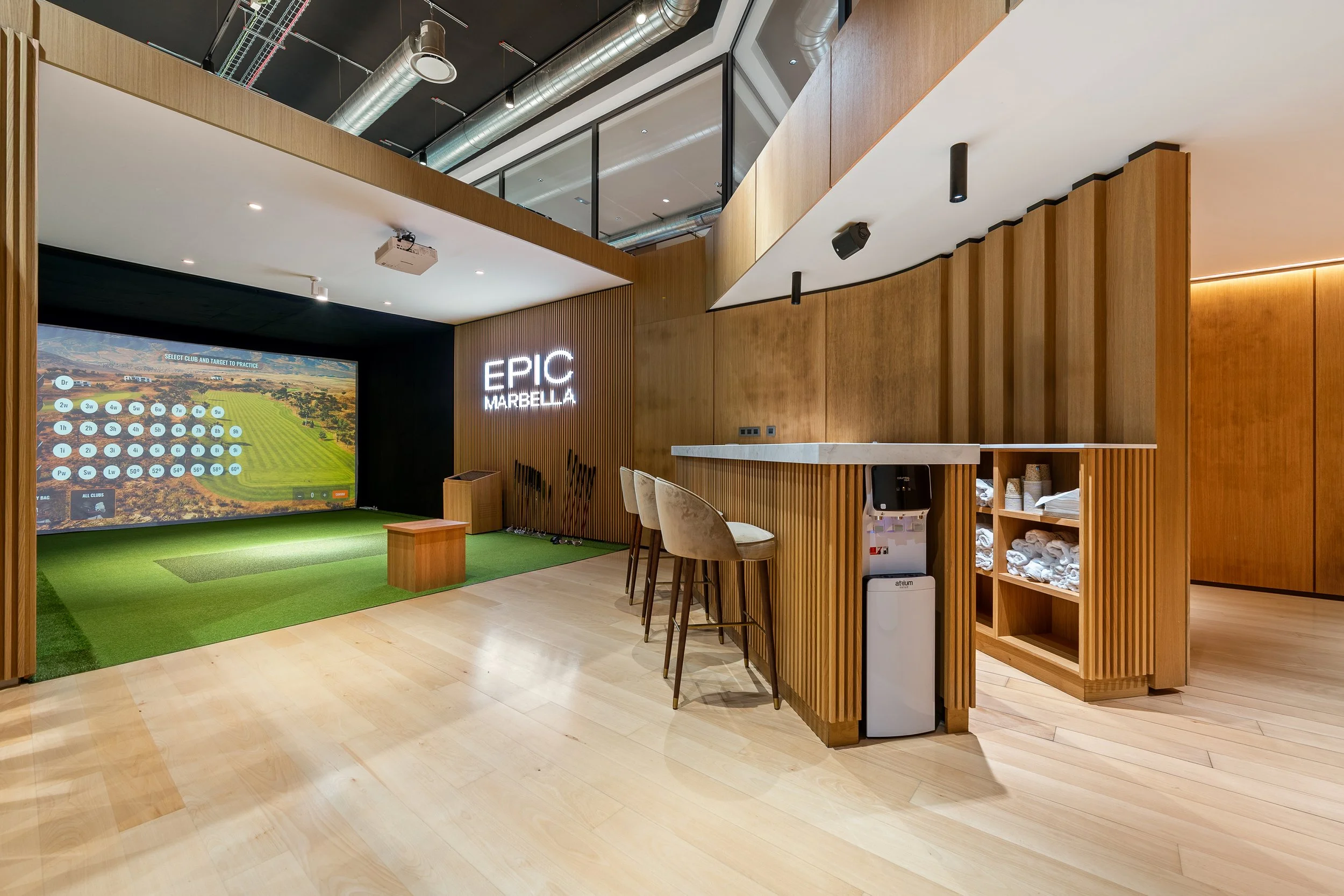 A dedicated entertainment or "social club" room featuring a high-tech golf simulator, a sleek wooden bar area with stools, and integrated shelving.