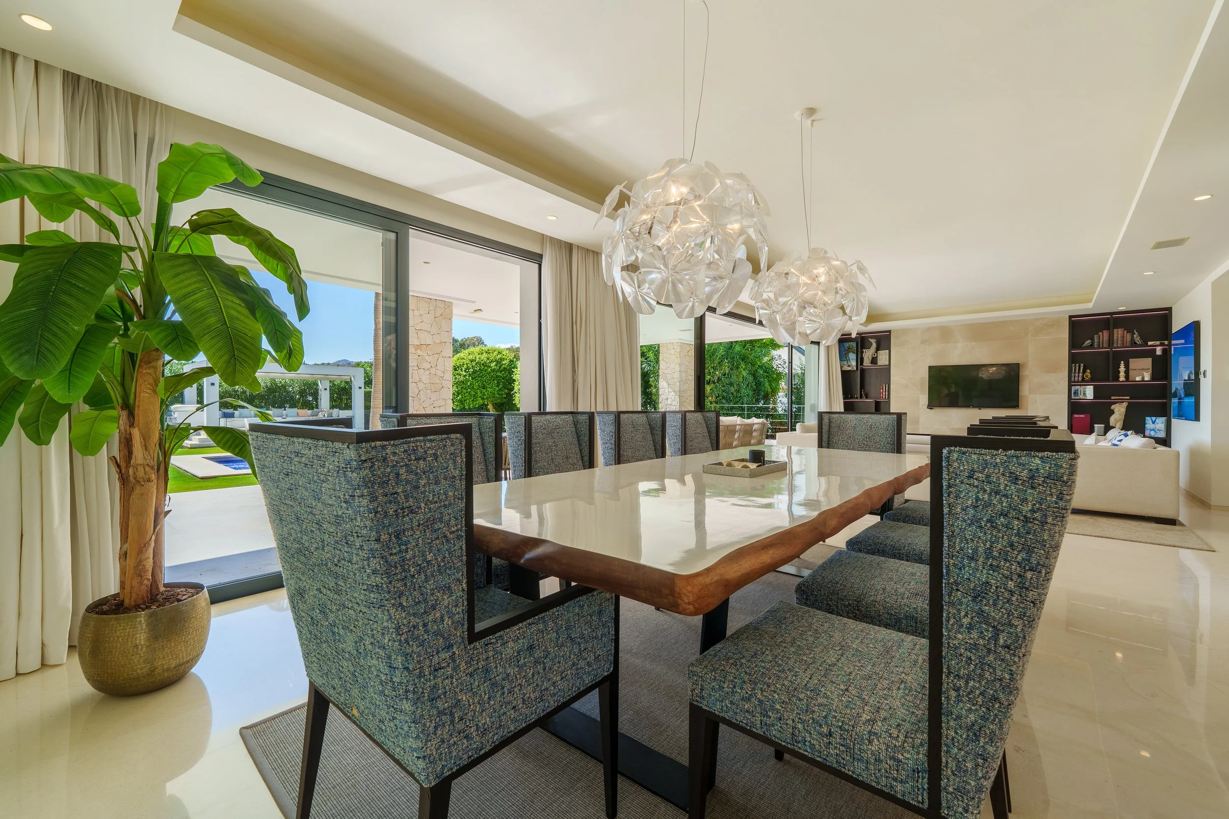 Elegant formal dining room with designer light fixtures, high-backed grey chairs, and views of the private Mediterranean gardens