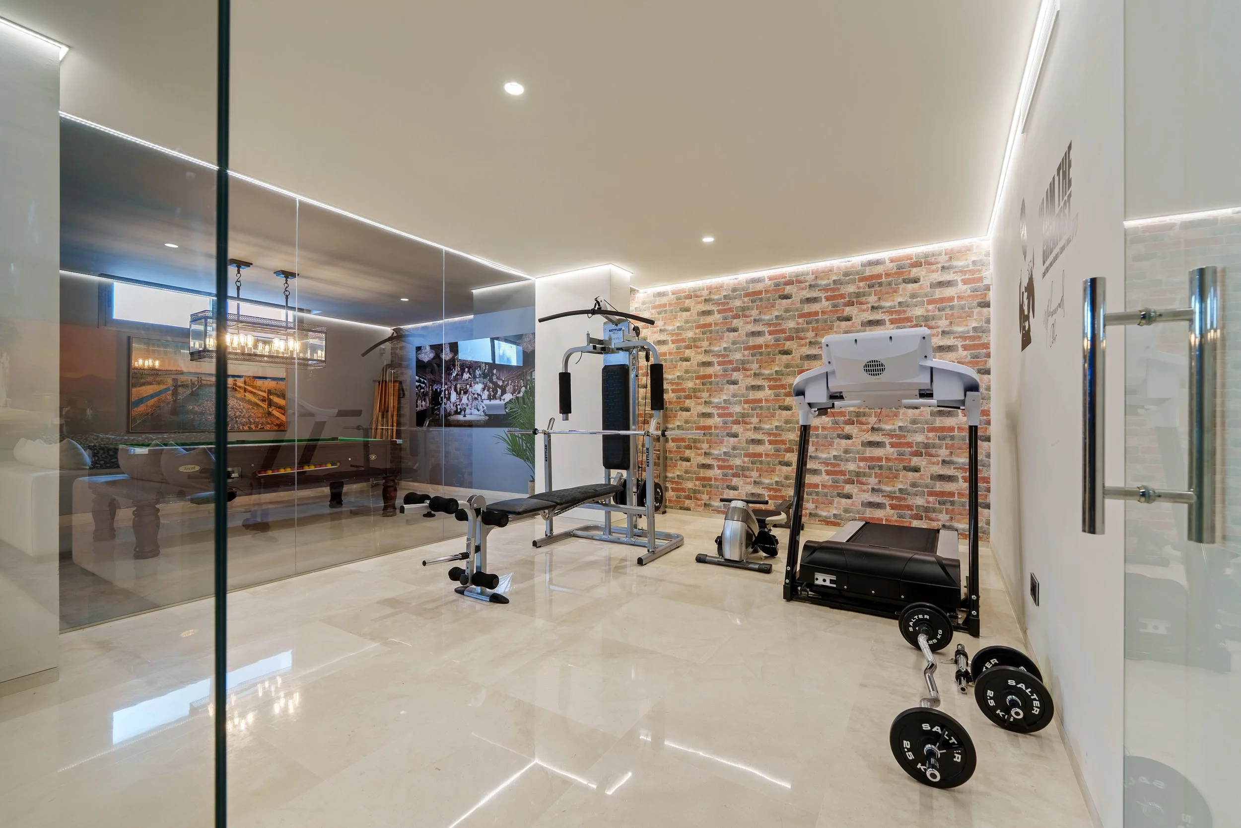 State-of-the-art glass-encased home gym with professional fitness equipment and natural stone feature wall.