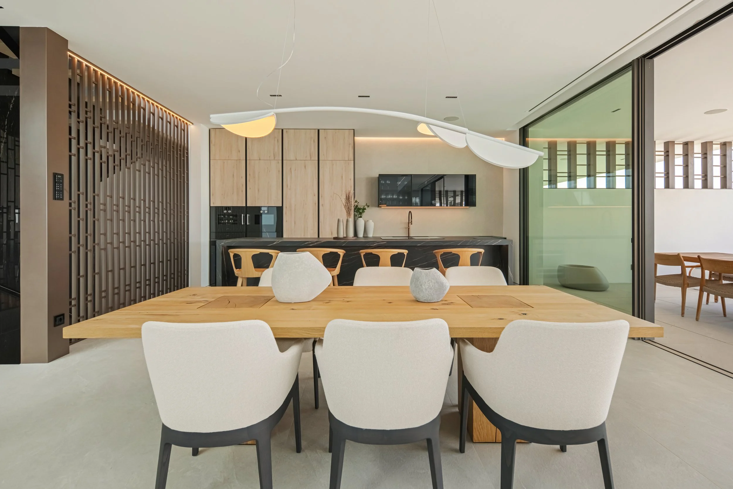 Open-plan dining space with a designer wooden table and modern lighting, seamlessly connected to the kitchen.