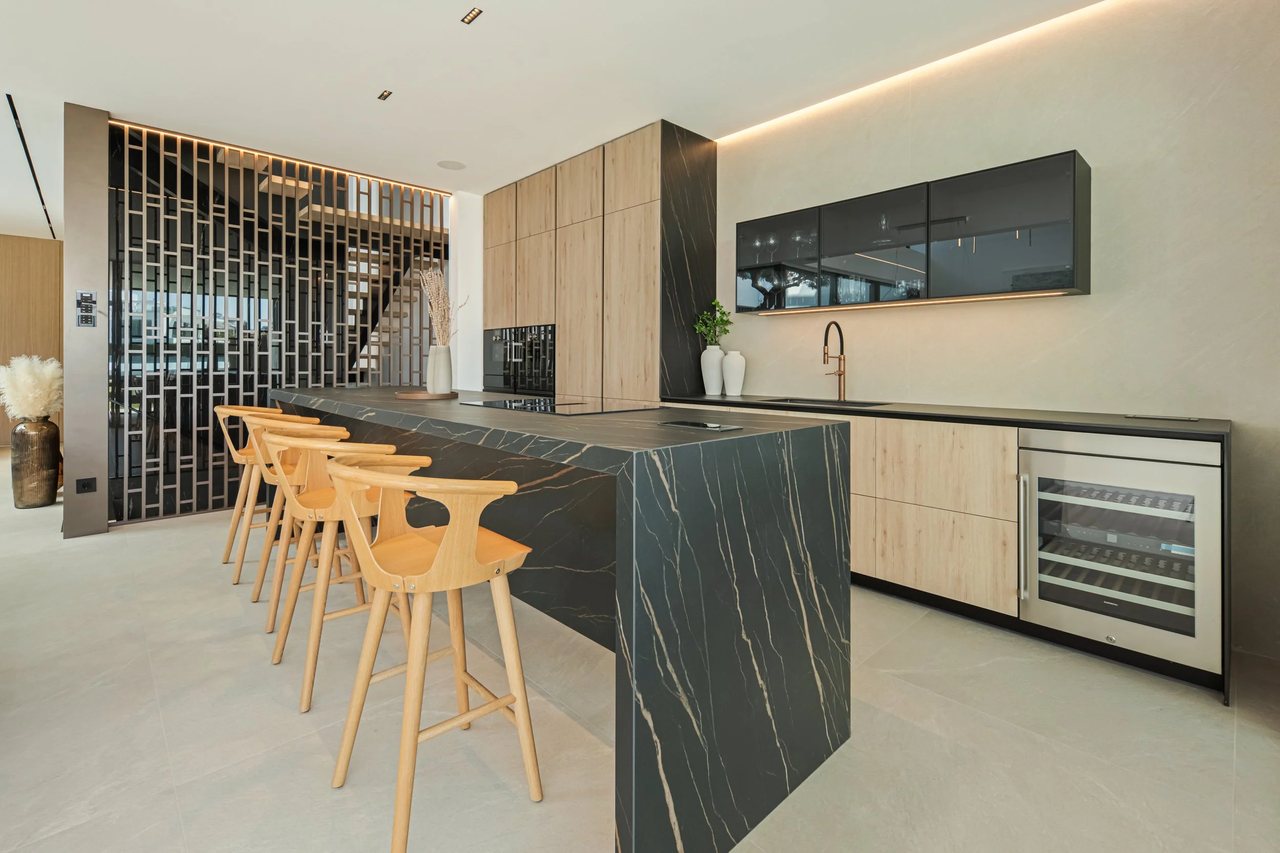 Sleek, minimalist kitchen featuring a dark stone island with breakfast bar and premium integrated wine cooler.