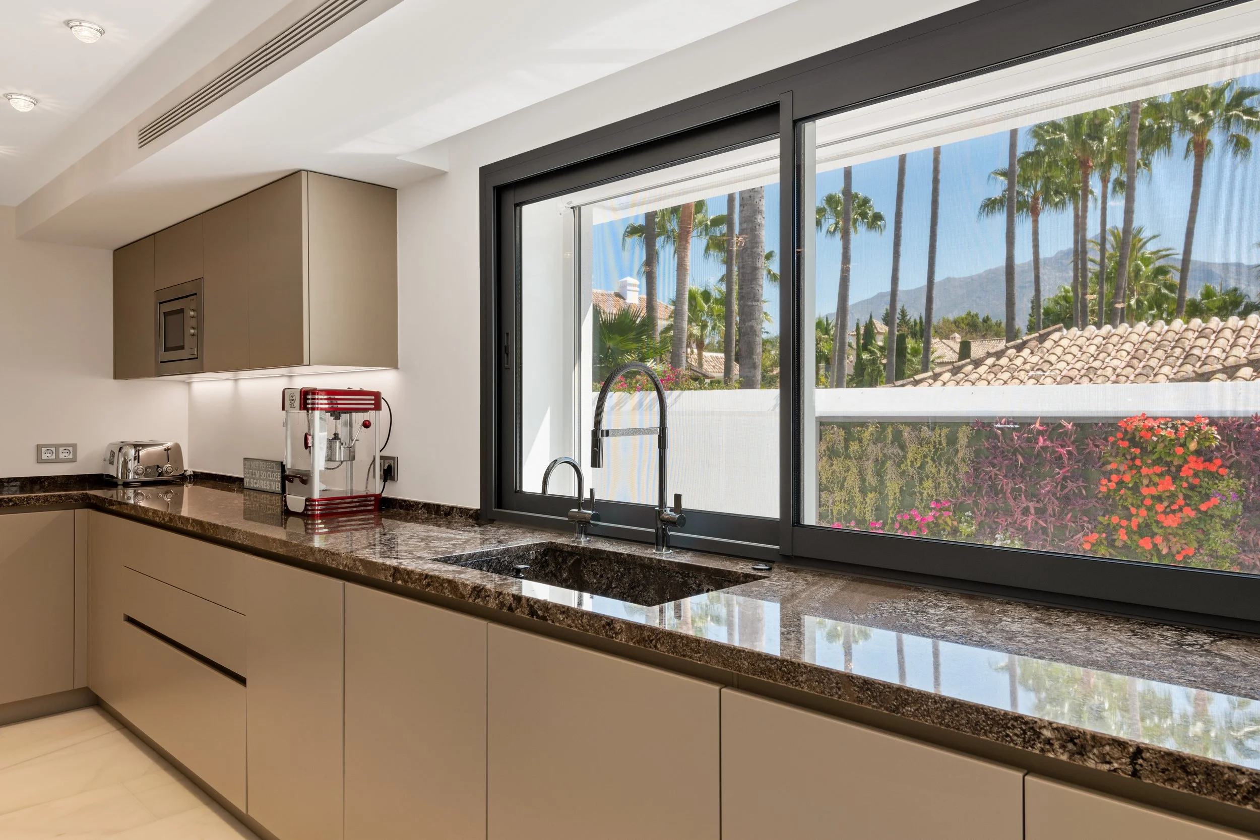 Designer kitchen with taupe cabinetry marble countertops and open plan dining area Nueva Andalucia Ref CMH2440