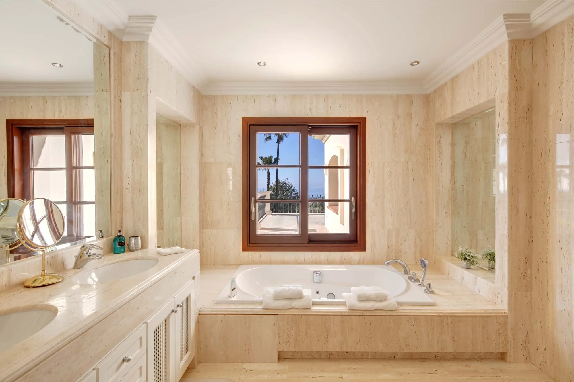Principal ensuite bathroom wrapped in cream marble with a built-in Jacuzzi tub and sea view window.
