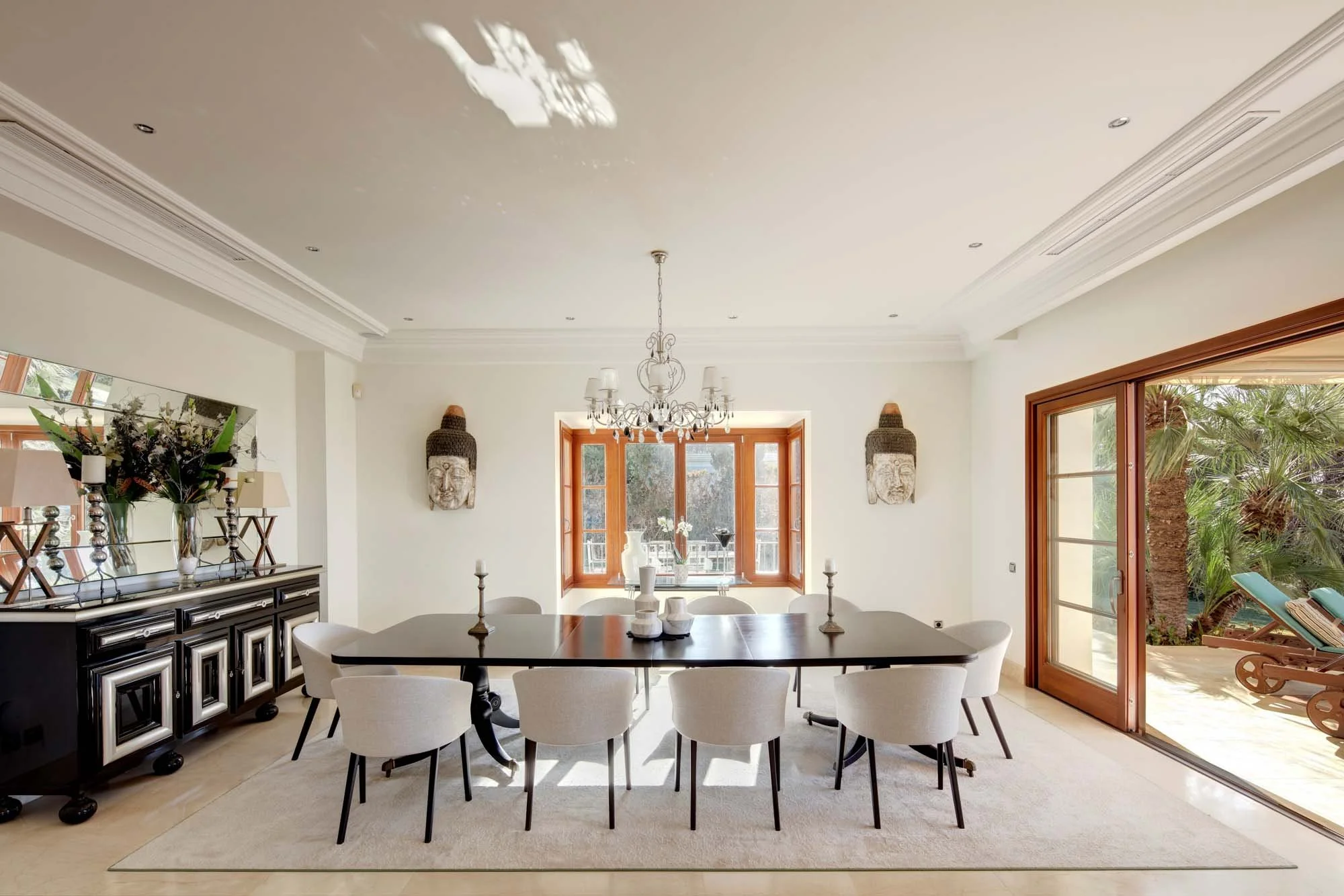 Luxury formal dining room with statement crystal chandelier and large wood-framed windows.