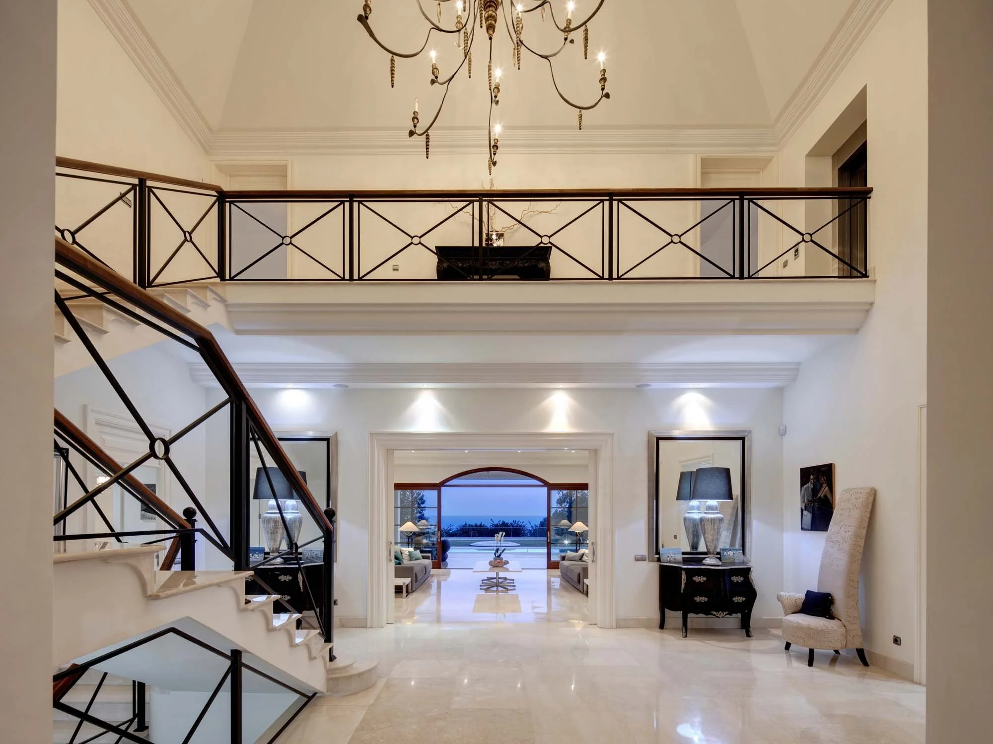 Grand double-height reception hall with marble floors, staircase, and natural light.