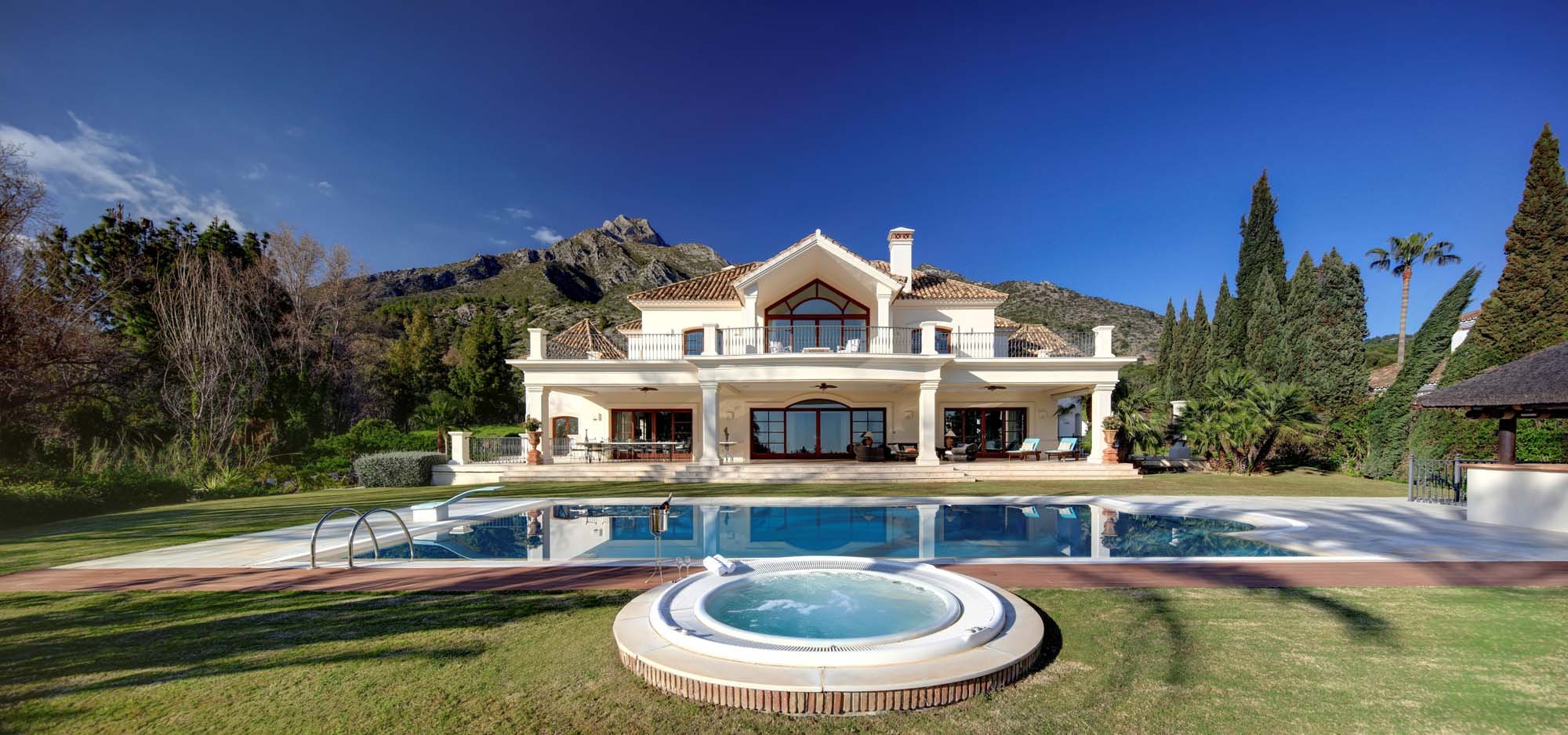 Illuminated contemporary mansion and circular outdoor Jacuzzi pool at twilight.