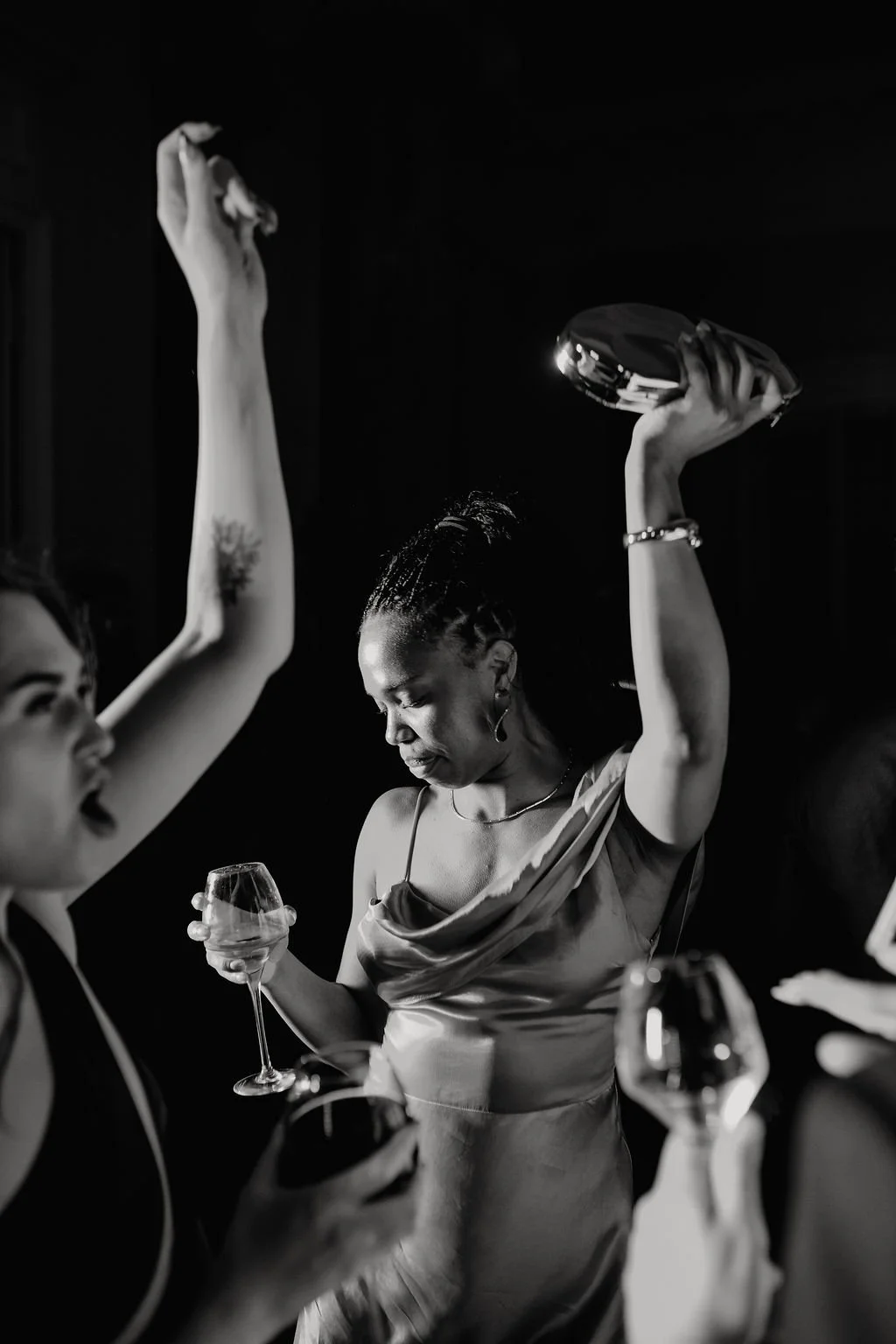 Black and white photo of women dancing and holding wine glasses at a social gathering or party.