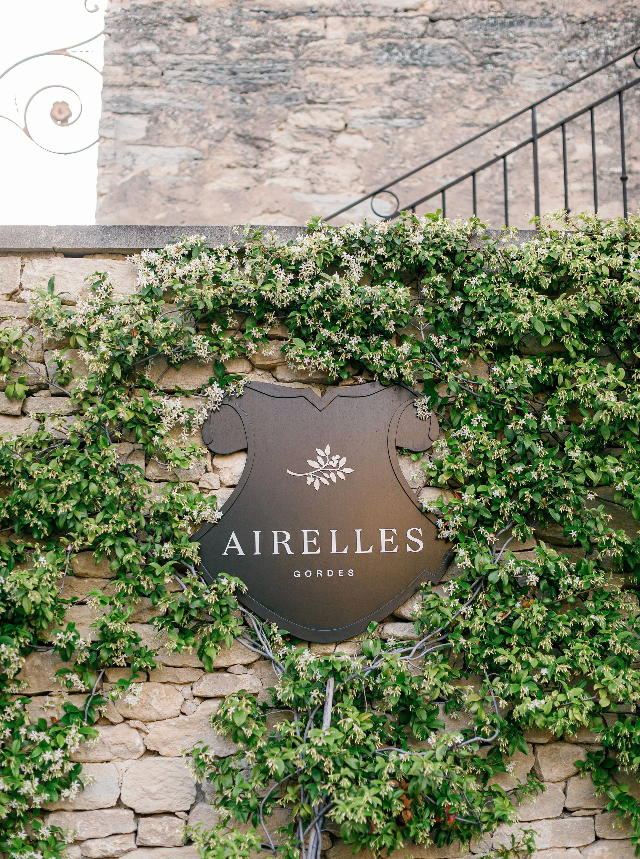 A decorative sign with the name 'Airelles Gordes' on a rustic stone wall surrounded by green climbing plants with small white flowers.