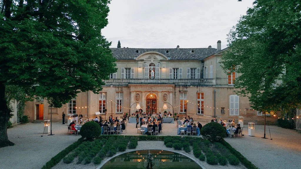 Outdoor evening wedding at Chateau Martinay in Provence with guests seated at tables, string lights, and large trees surrounding the area.
