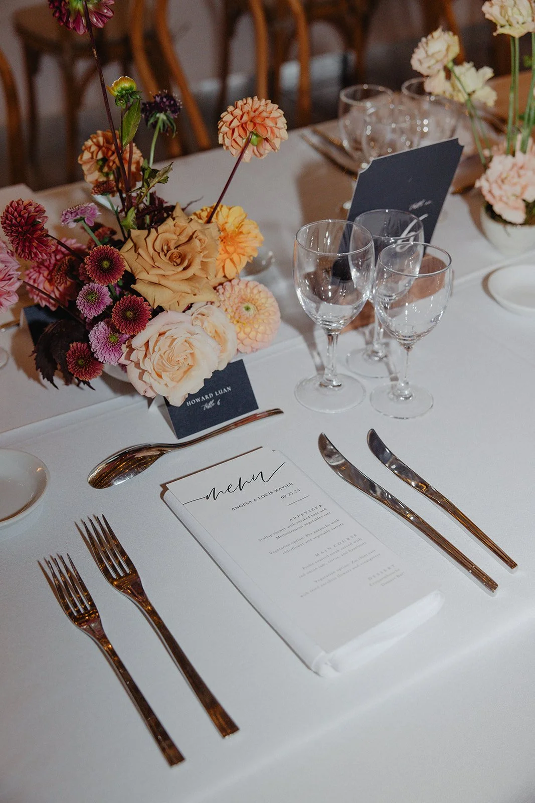 Elegant wedding table setting with a floral centerpiece, four wine glasses, a menu, and neatly arranged silverware.