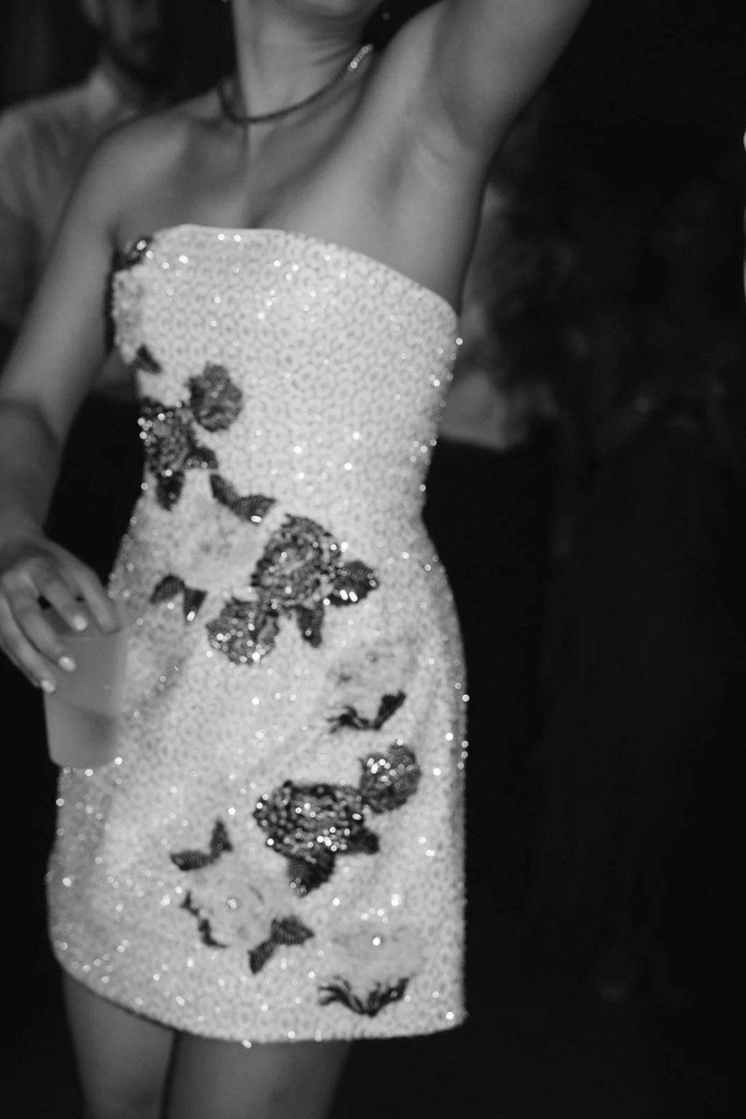 Close-up of the bride wearing a strapless, sequined, floral-patterned dress, holding a drink in her hand at her wedidng on the dancefloor.