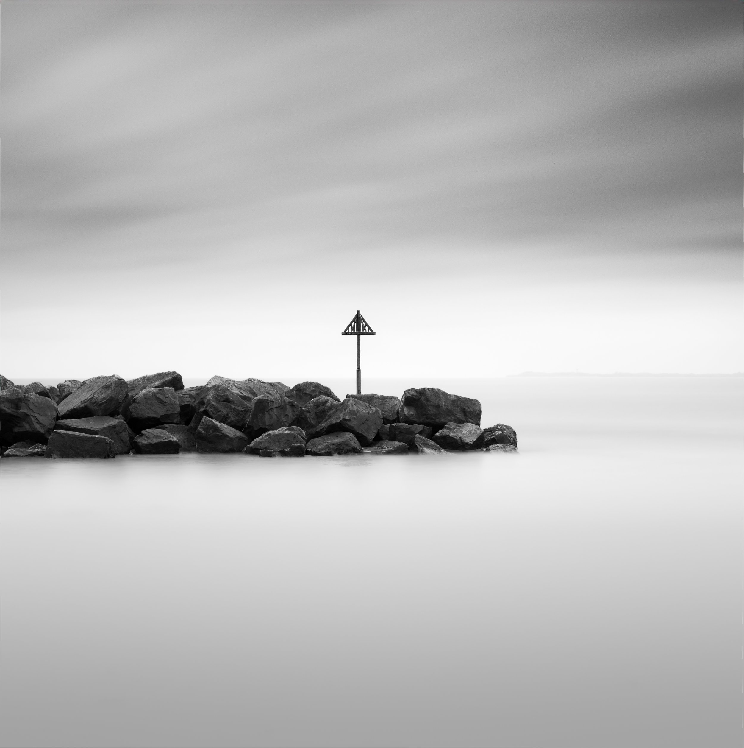 black and white long exposure fine art minimal image of a coastal marker and sea defence 