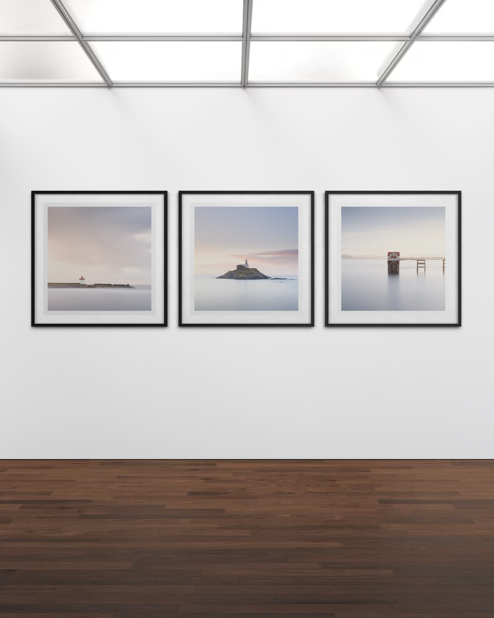 Three framed seascape photographs on a white gallery wall with a wooden floor and a skylight ceiling.