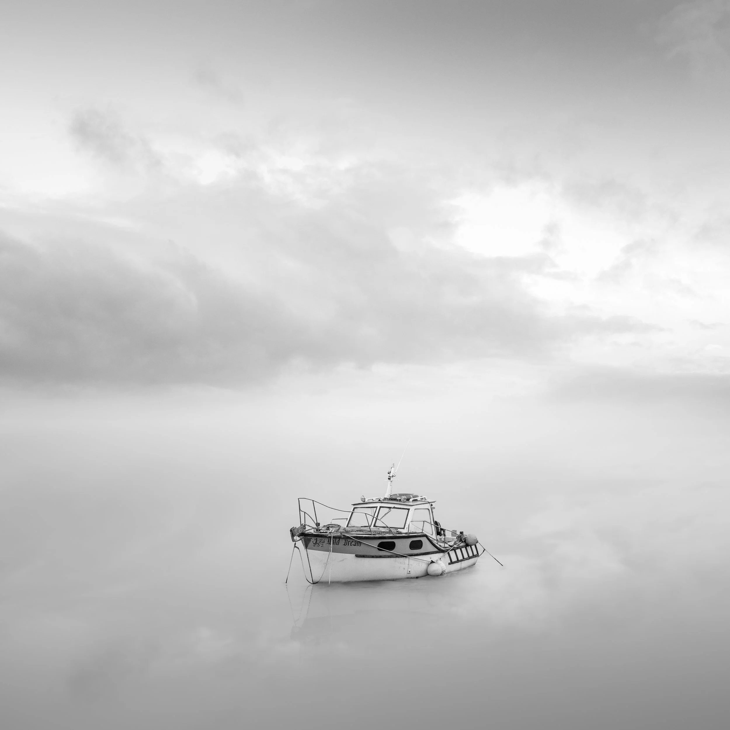 Black and white photo of a boat named 'Wild Dream' floating on calm water with overcast sky and no visible waves.