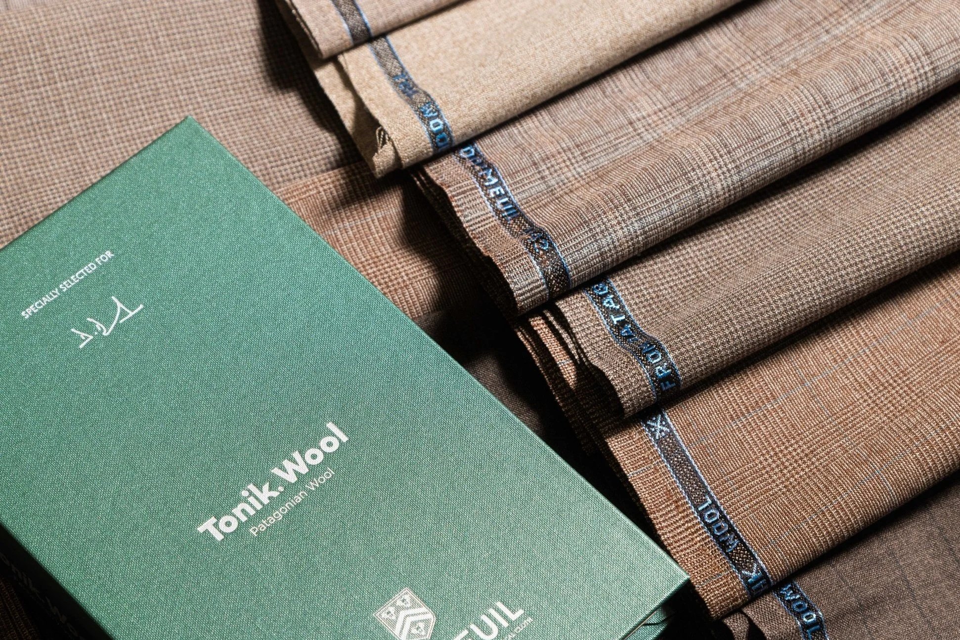 Several folded fabric swatches in shades of brown with a box of Tonik Wool fabric from Palagonia Wool in the foreground.