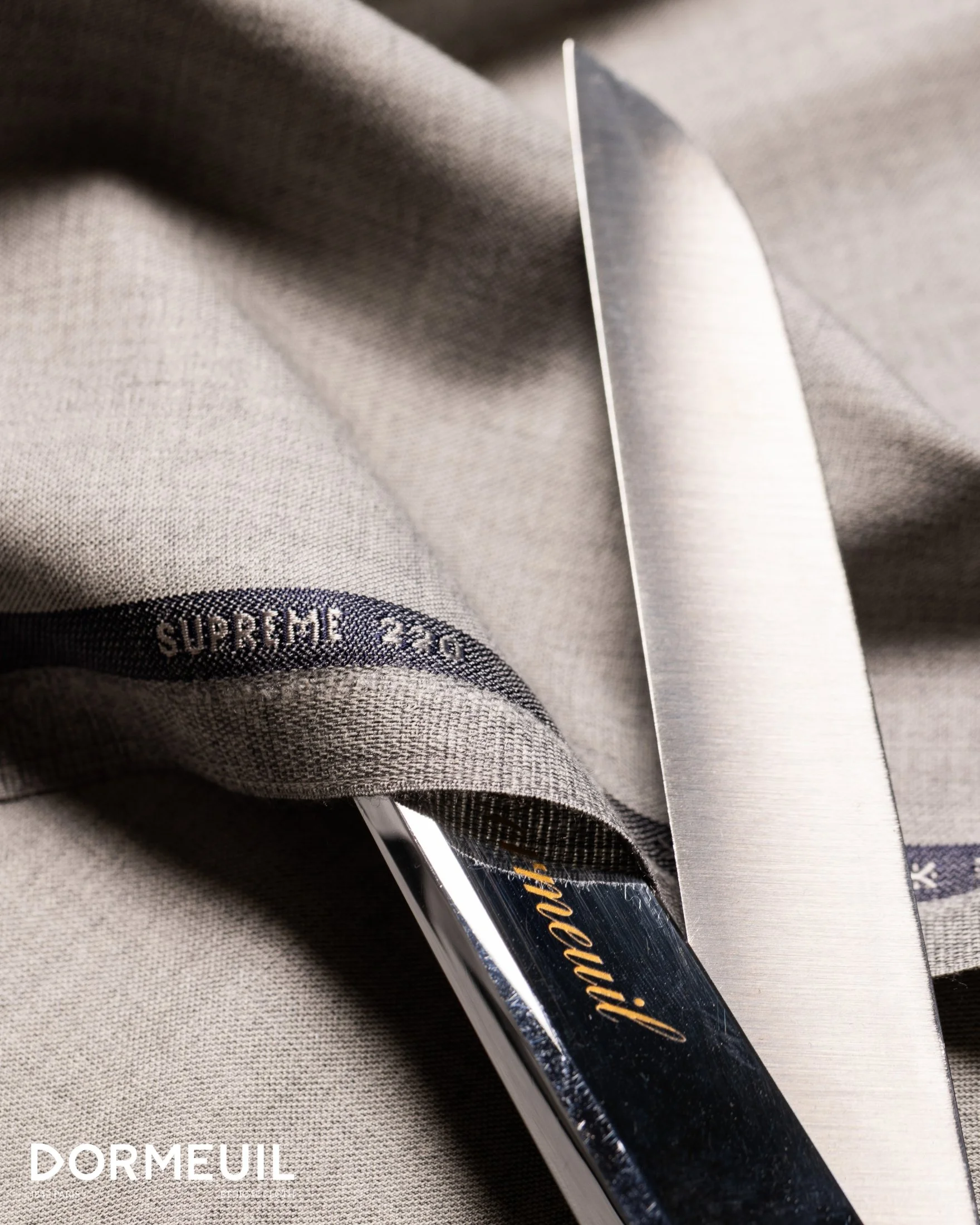 Close-up of a gray Supreme x North Face fabric, a knife cutting through the fabric, with a hint of the word 'Dormeur' and a showing 'supreme 20' label.