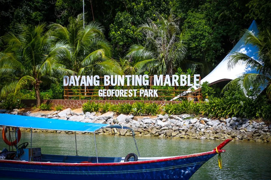 Sign for Dayang Bunting Marble at Geoforest Park, with lush greenery and a boat in the water