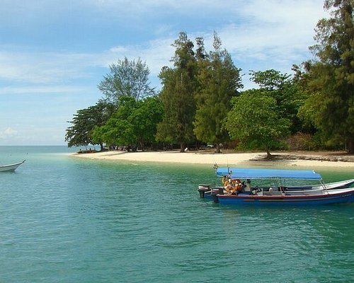 A tropical beach with turquoise water, a small boat anchored near the shore, and lush green trees in the background.