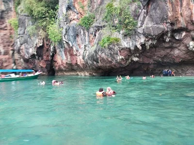 People swimming and floating in clear turquoise water near a rocky cliff.
