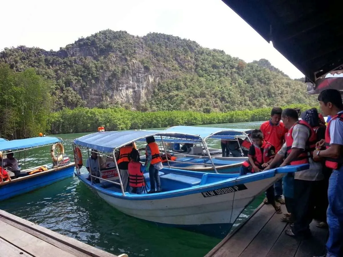 Group of people in life jackets boarding or disembarking from boats on a river with lush green trees and rocky hills in the background.