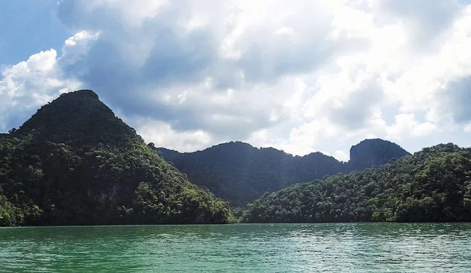 Scenic view of a lake surrounded by lush green mountains with a partly cloudy sky overhead.