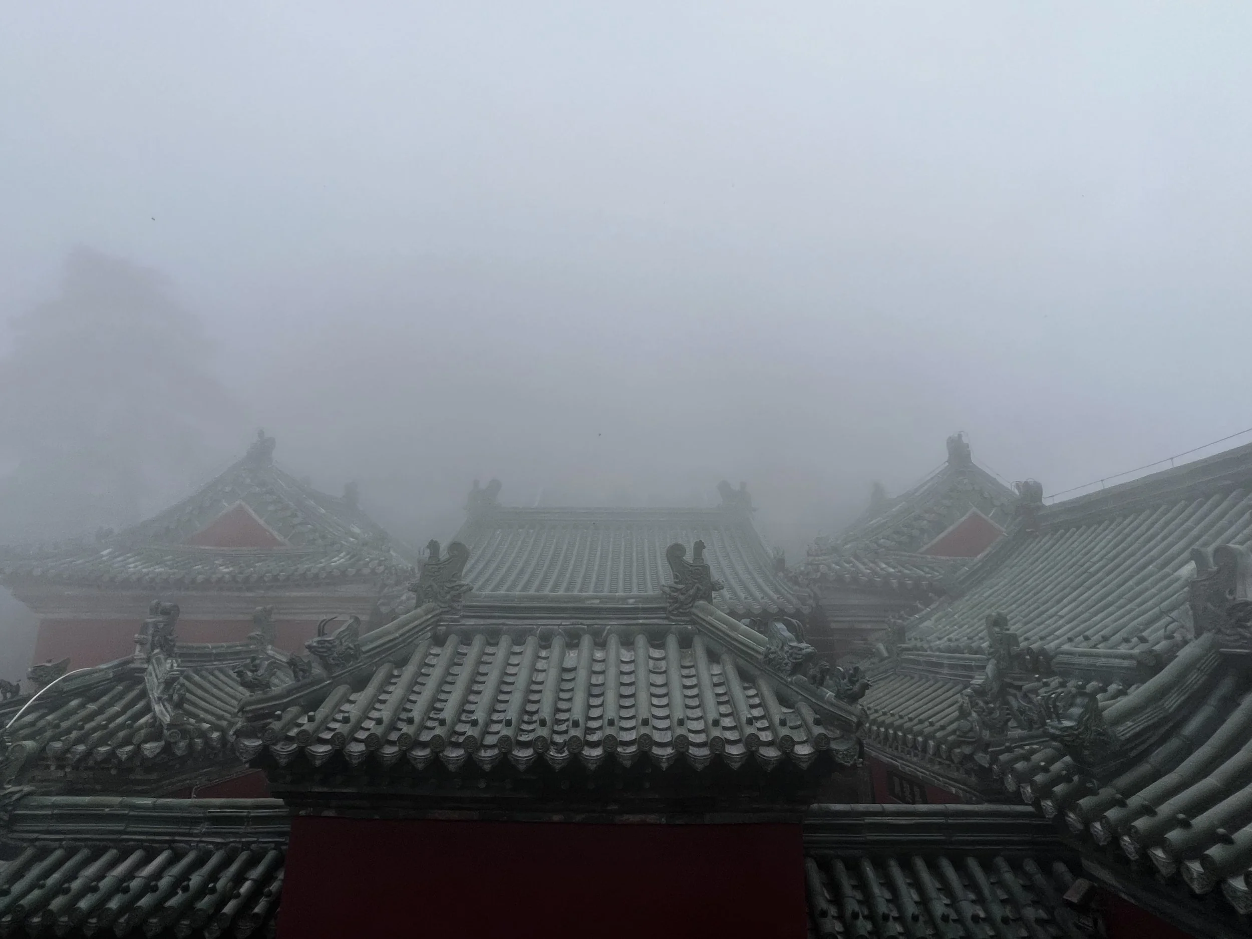 View of traditional Asian temple rooftops with ornate details, shrouded in fog.
