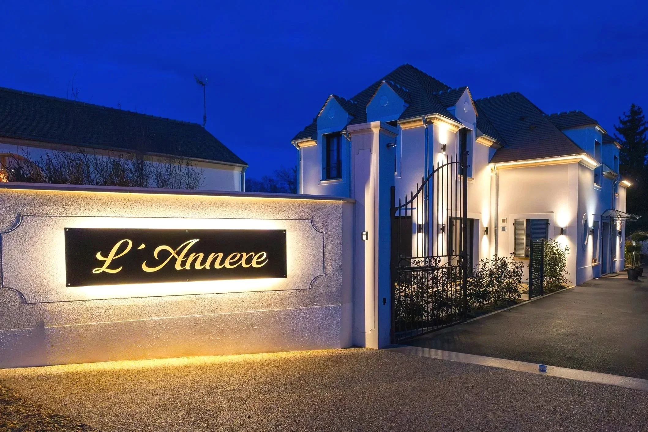 Façade d'une maison élégante éclairée la nuit avec un mur portant un panneau lumineux indiquant 'L'Annexe'.