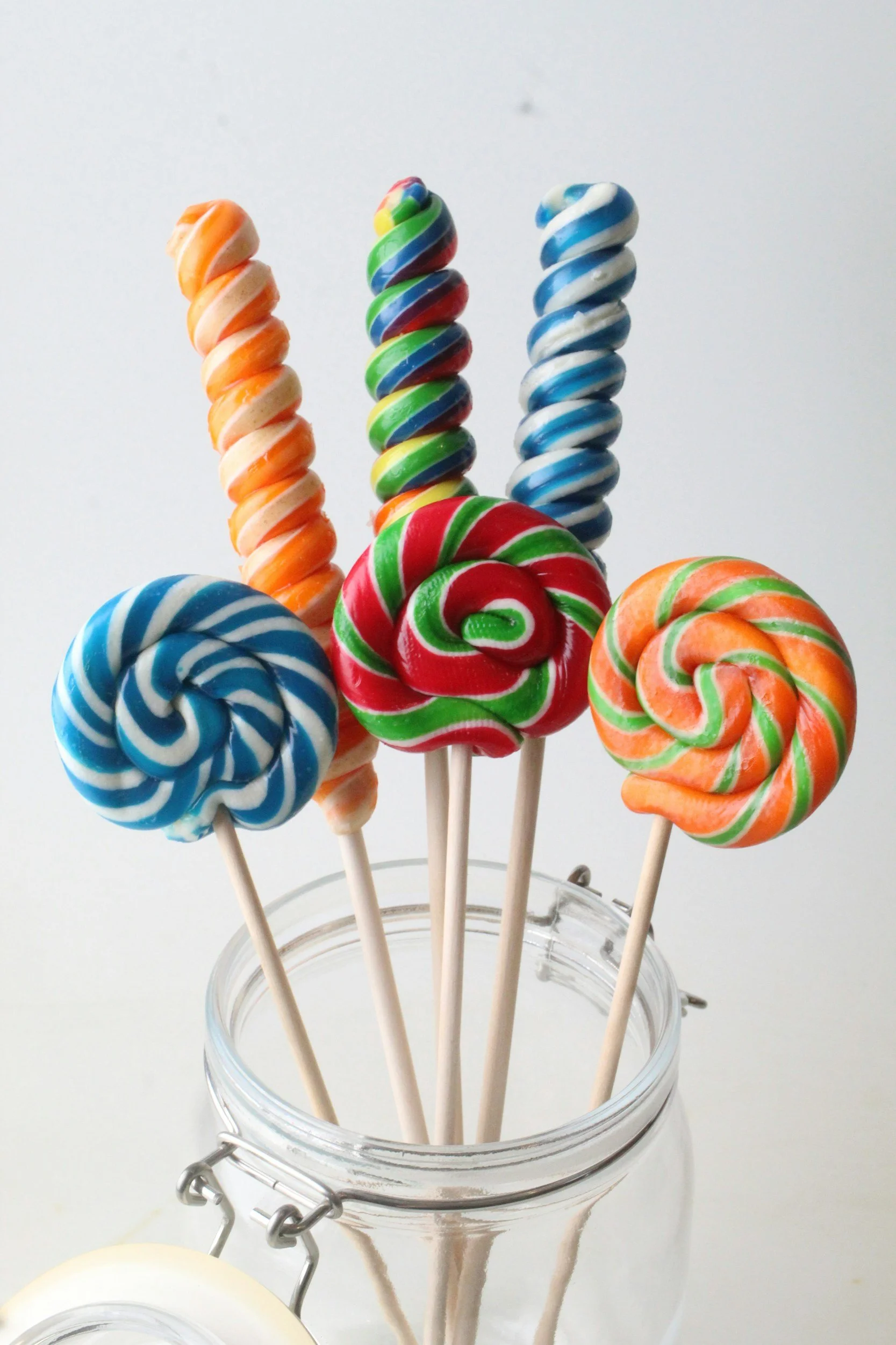 Colored swirl lollipops in a glass jar against a light background.