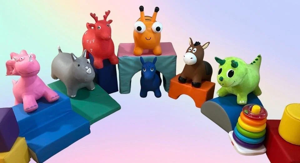 Colorful plastic animal toys arranged in a semi-circle on a rainbow-colored toy staircase against a light pink background.